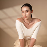 Enhance your style with this elegant Heart Pearl Chain Necklace, beautifully complemented by a woman in a chic white top and pants seated on a chair