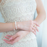 A woman in a white dress adorned with a stunning bracelet of freshwater pearls and 18k yellow gold on her wrist.