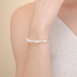  A woman in a white dress adorned with a stunning pearl bracelet made of freshwater pearls and 18k yellow gold.