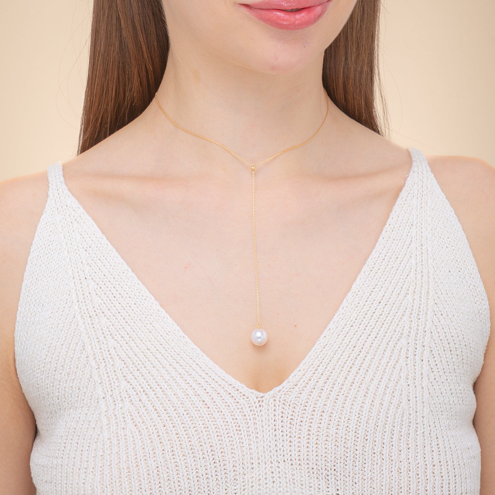 A woman elegantly dressed in a white top, featuring a freshwater pearl necklace and chic 18k yellow gold details.