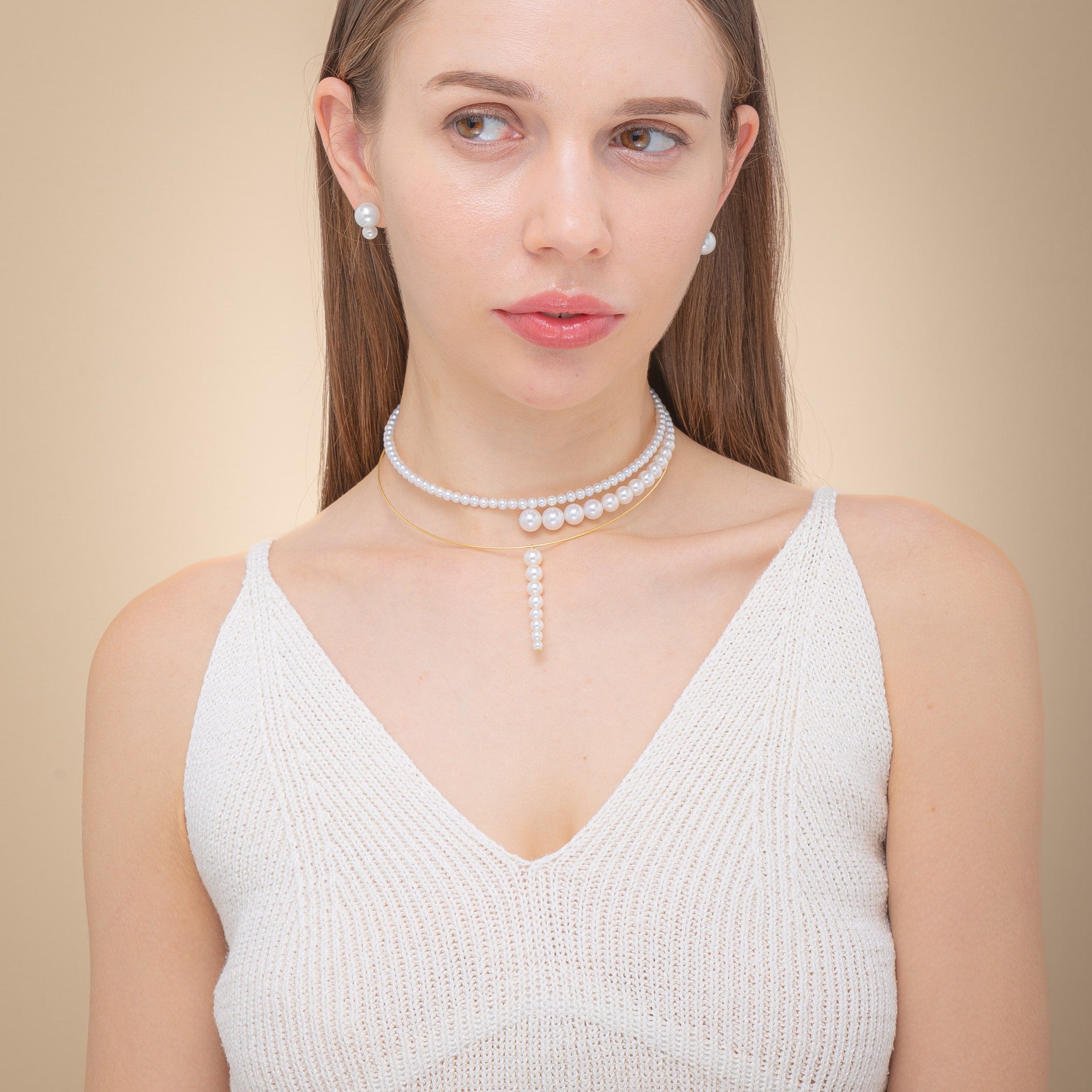 Woman in a chic white top, elegantly accessorized with a freshwater pearl necklace featuring 18K yellow gold accents.