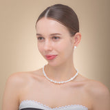 Elegant woman in a white dress, showcasing a freshwater pearl necklace with a silver clasp, radiating timeless beauty.