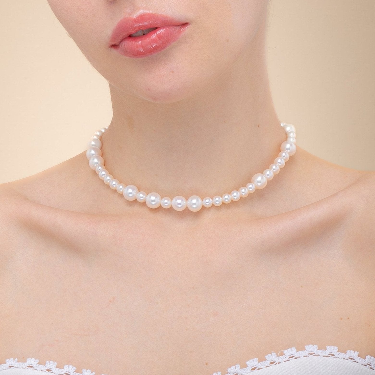 A woman in a white dress adorned with a freshwater pearl necklace featuring a silver clasp, exuding elegance and grace.